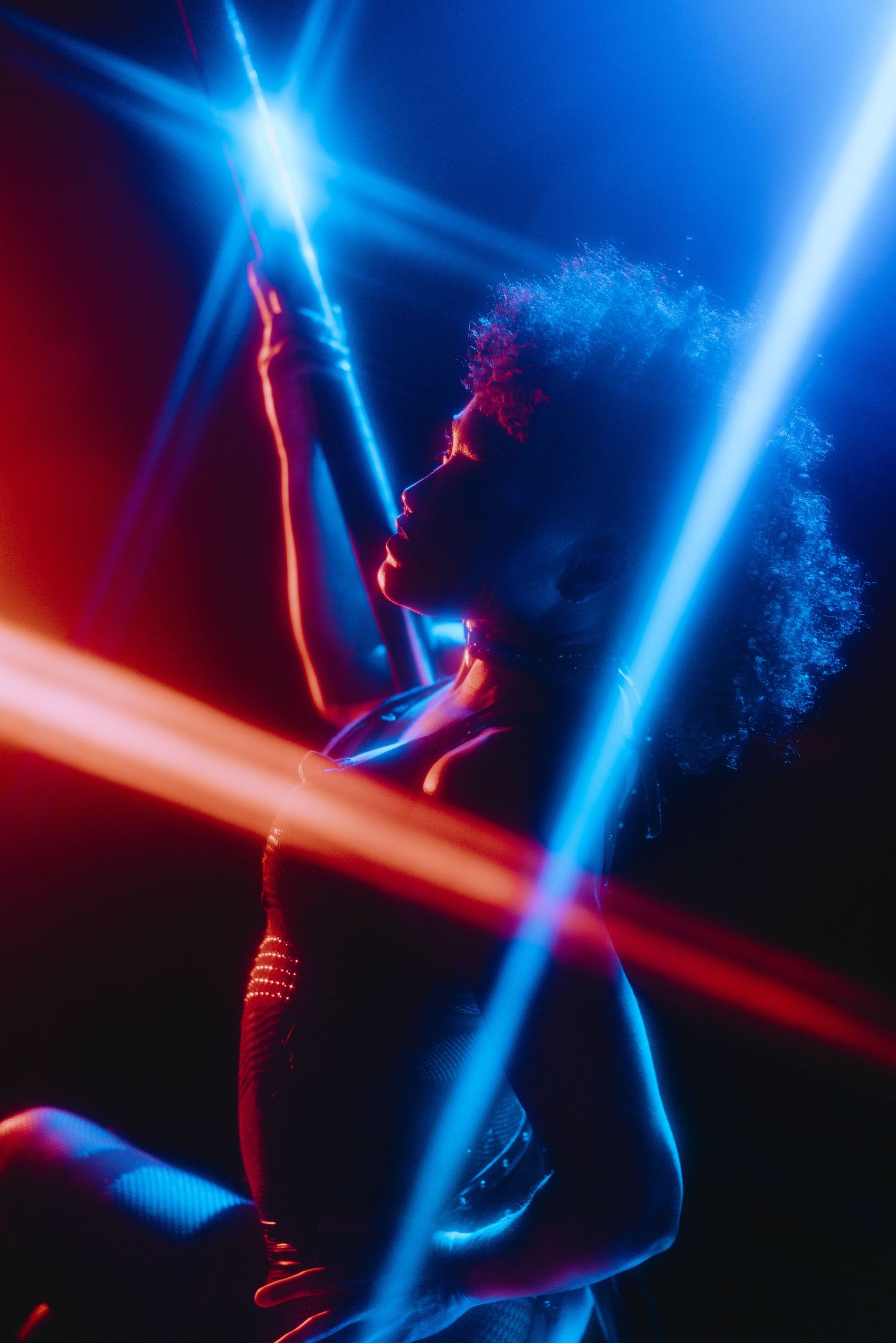 A pole dancer poses dramatically with vibrant blue and red laser beams crossing the dark stage.