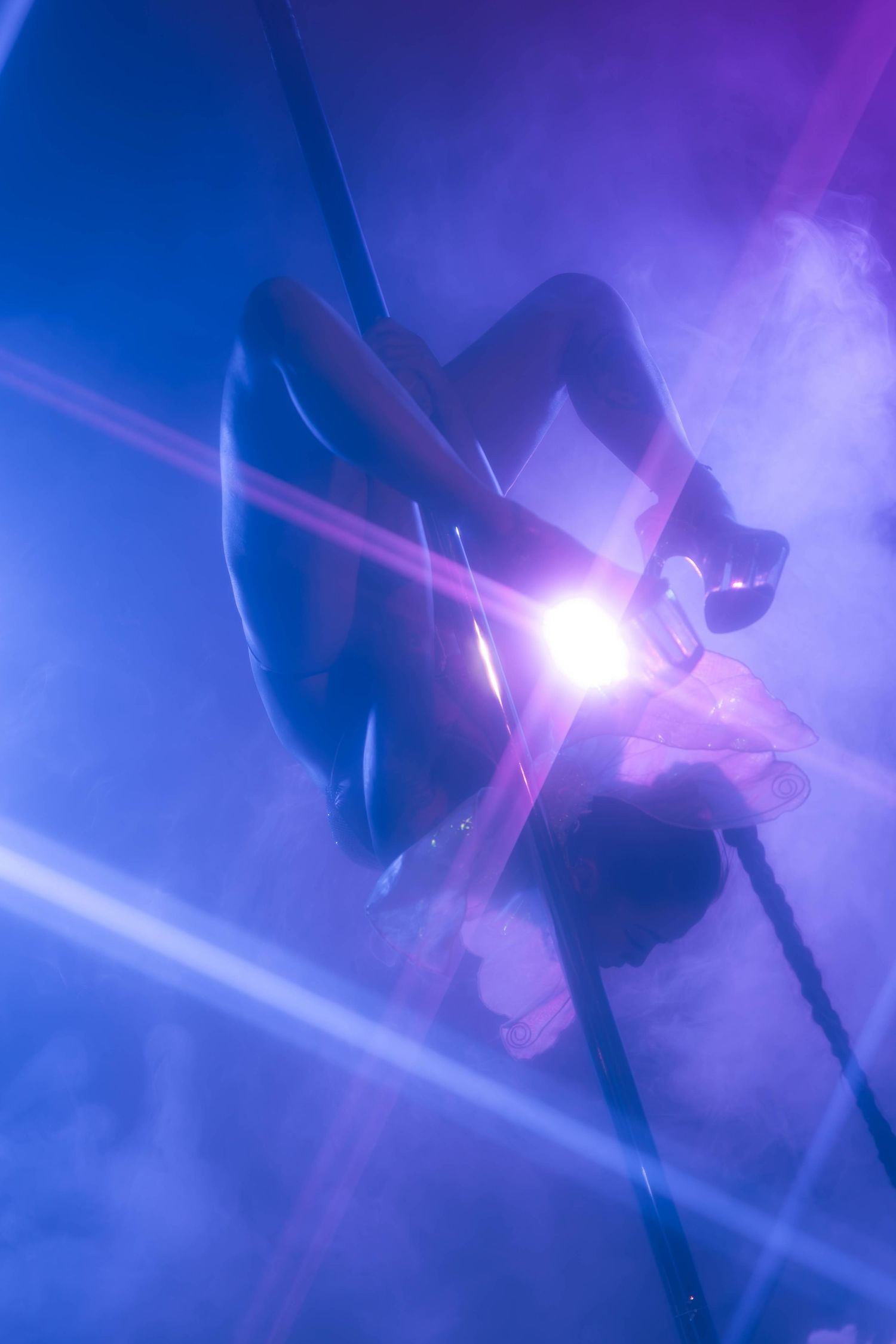 Aerial performer silhouetted against dramatic purple and blue stage lighting with lens flare and smoke effects.