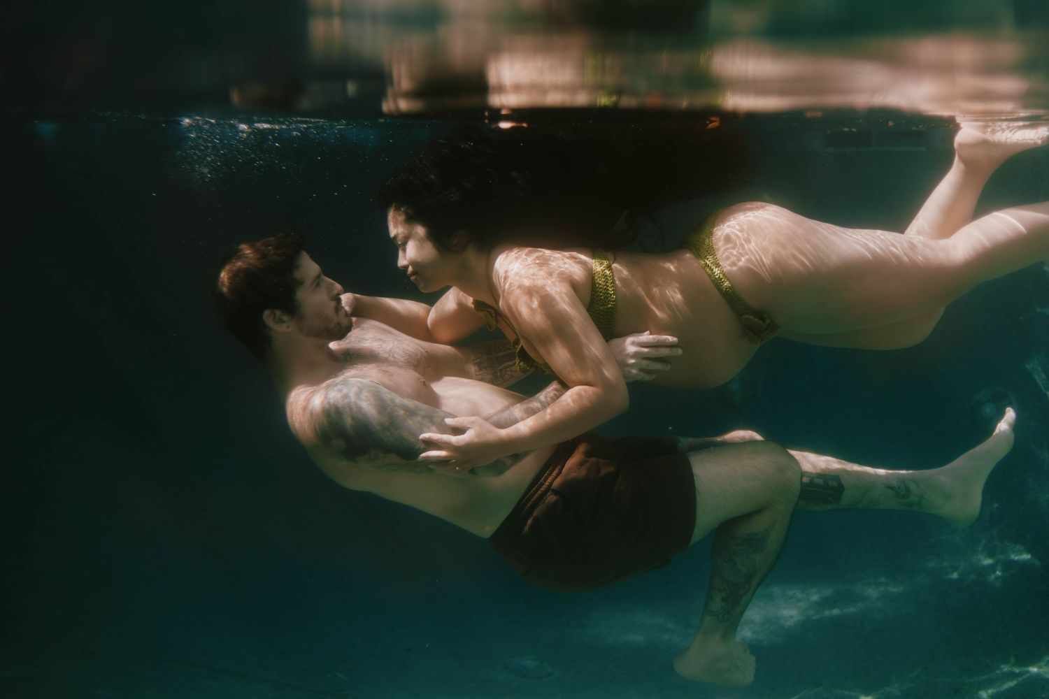 Couple embracing romantically underwater in a pool, captured in an artistic underwater photography shot.