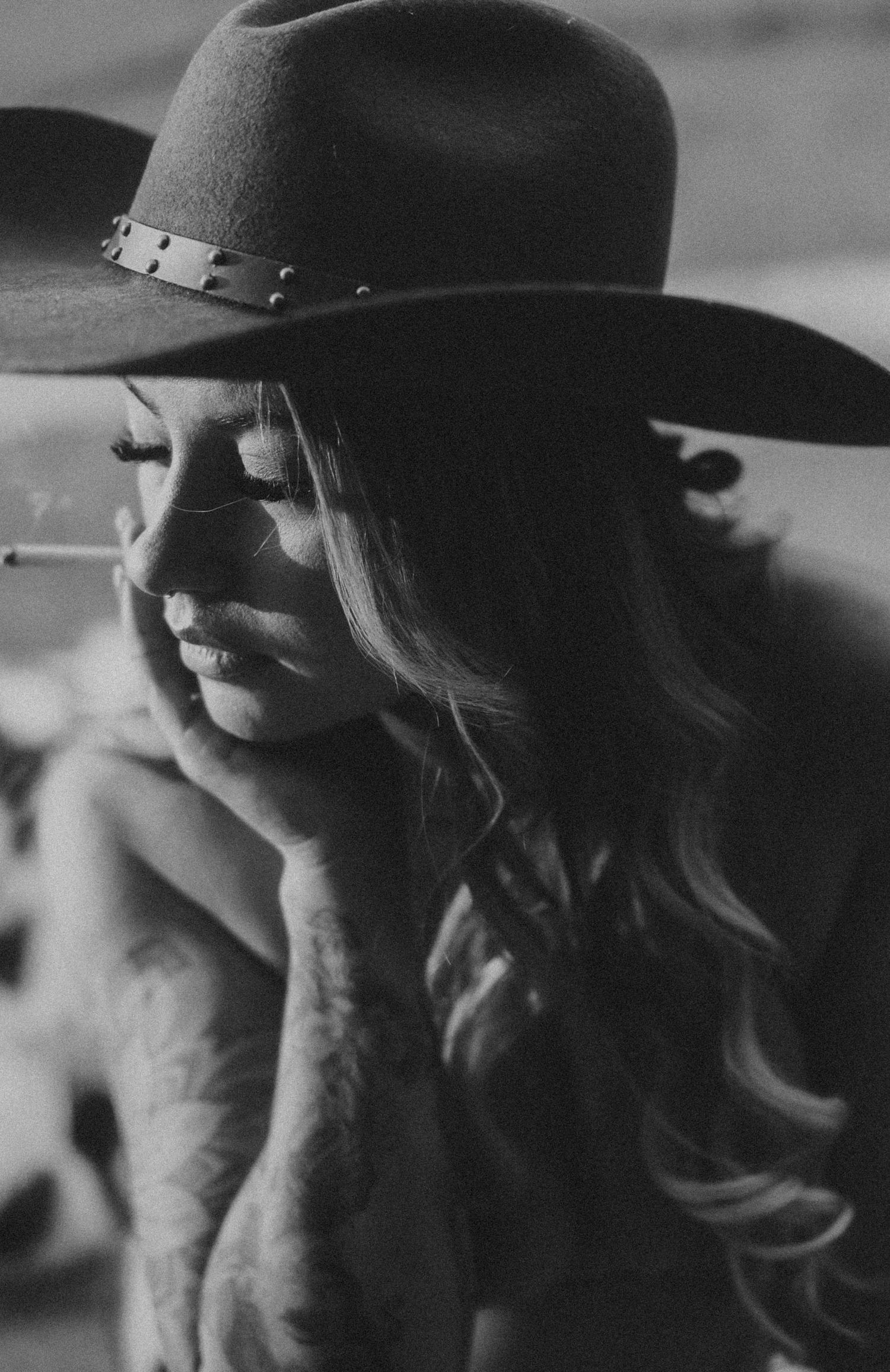 Black and white portrait of woman in cowboy hat smoking a cigarette.