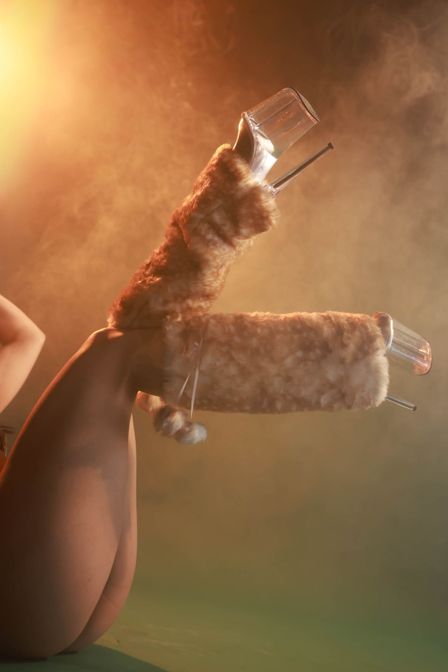 Nude figure holding fluffy roller with glass tubes in warm smoky light.