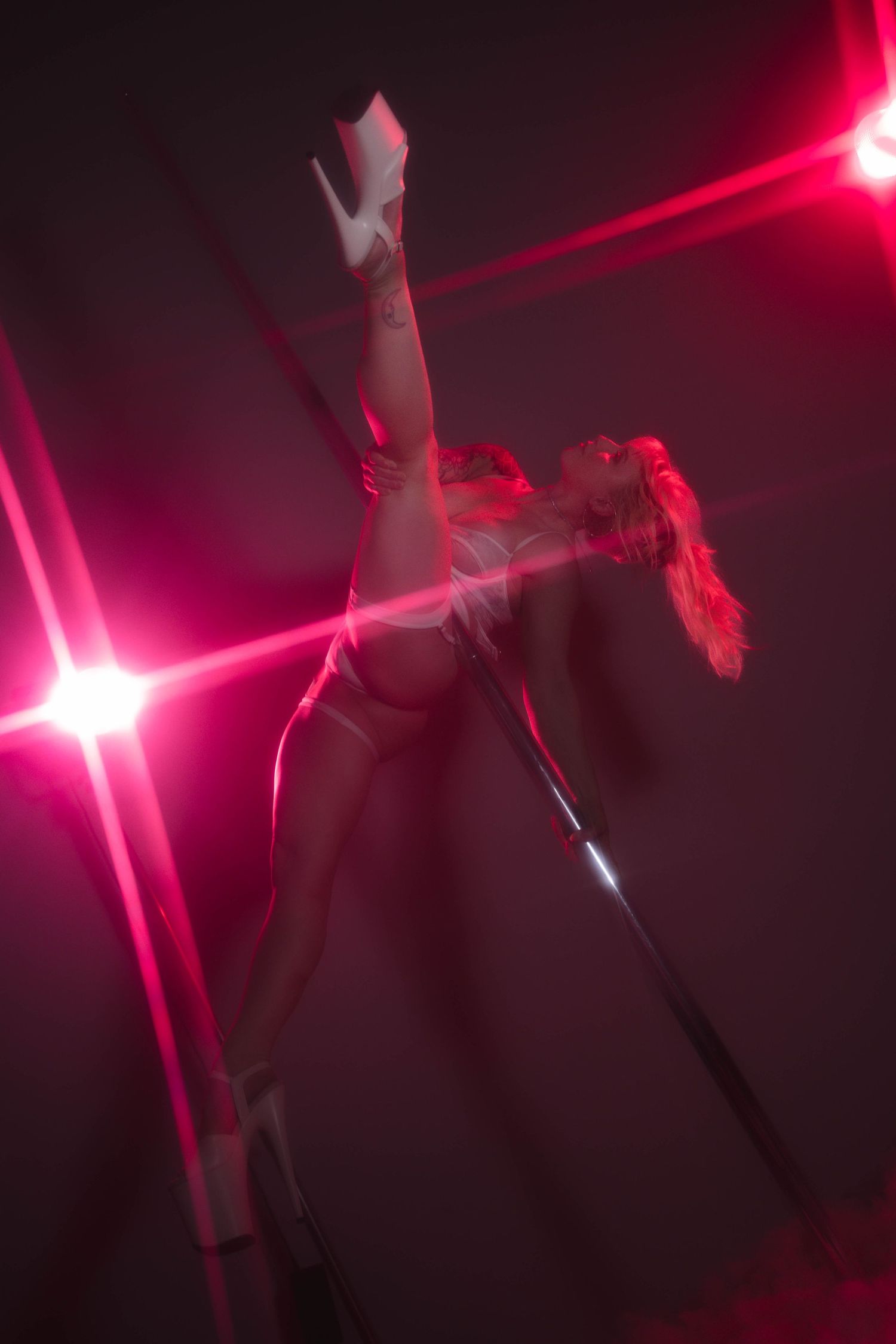 A pole dancer performs an athletic split under dramatic pink and red stage lighting.