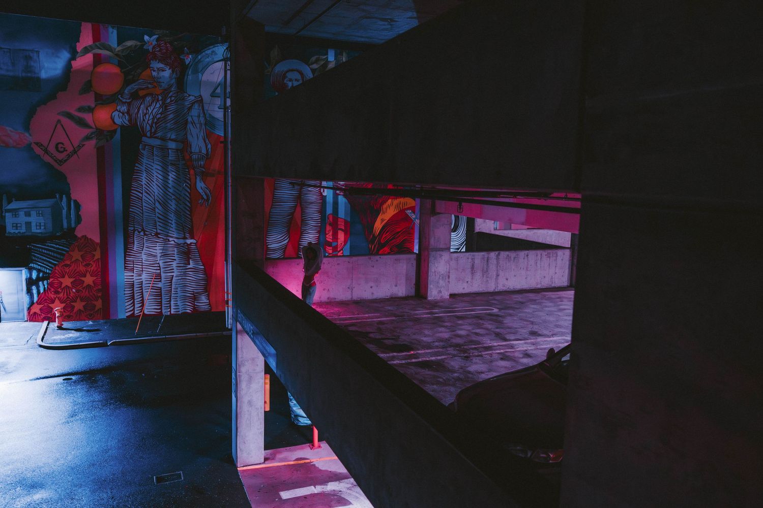 Dimly lit urban space featuring colorful murals and neon pink accent lighting below.