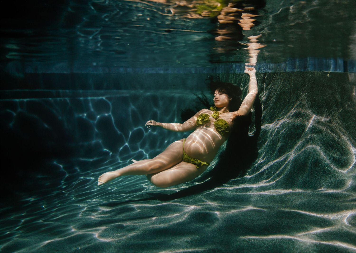 Pregnant woman in yellow bikini floating gracefully underwater in a pool, captured in a stunning maternity photo.