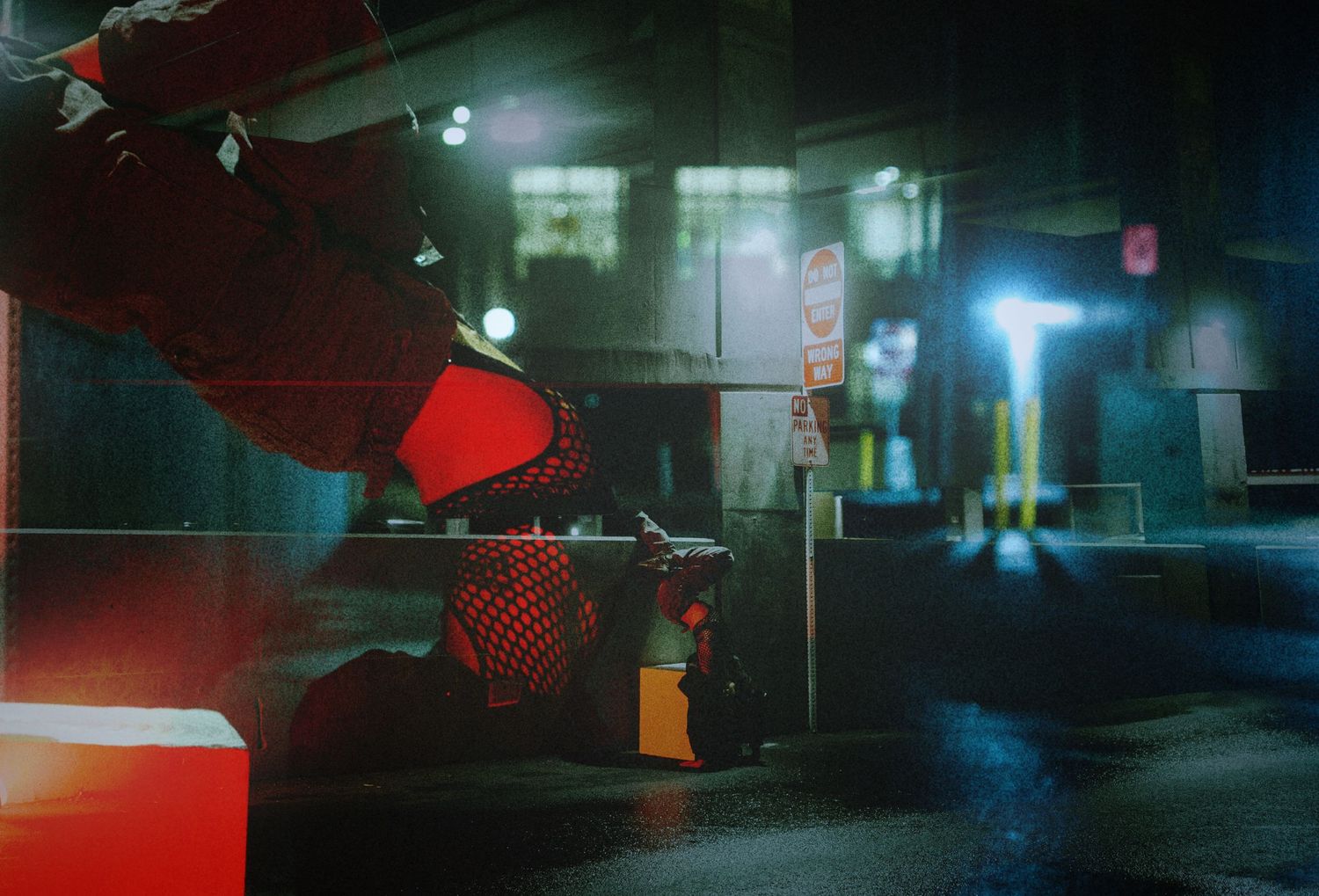 A figure in red suit stands in a dark, neon-lit urban alley at night, creating a cyberpunk atmosphere.