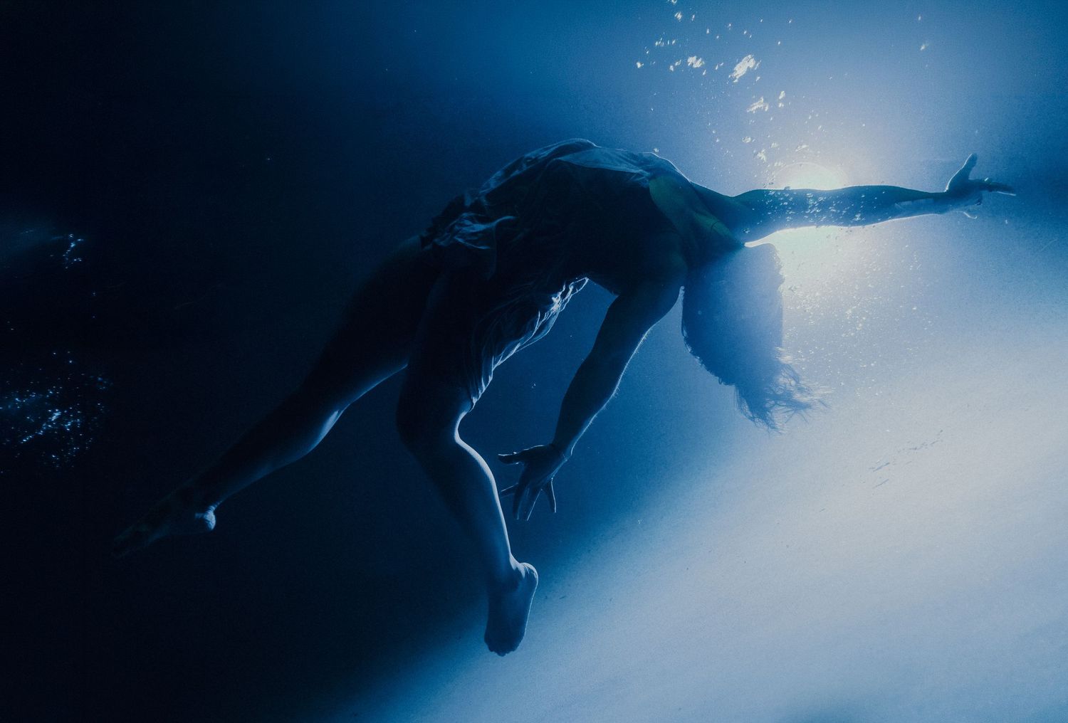 Underwater silhouette of a swimmer diving gracefully in deep blue water.