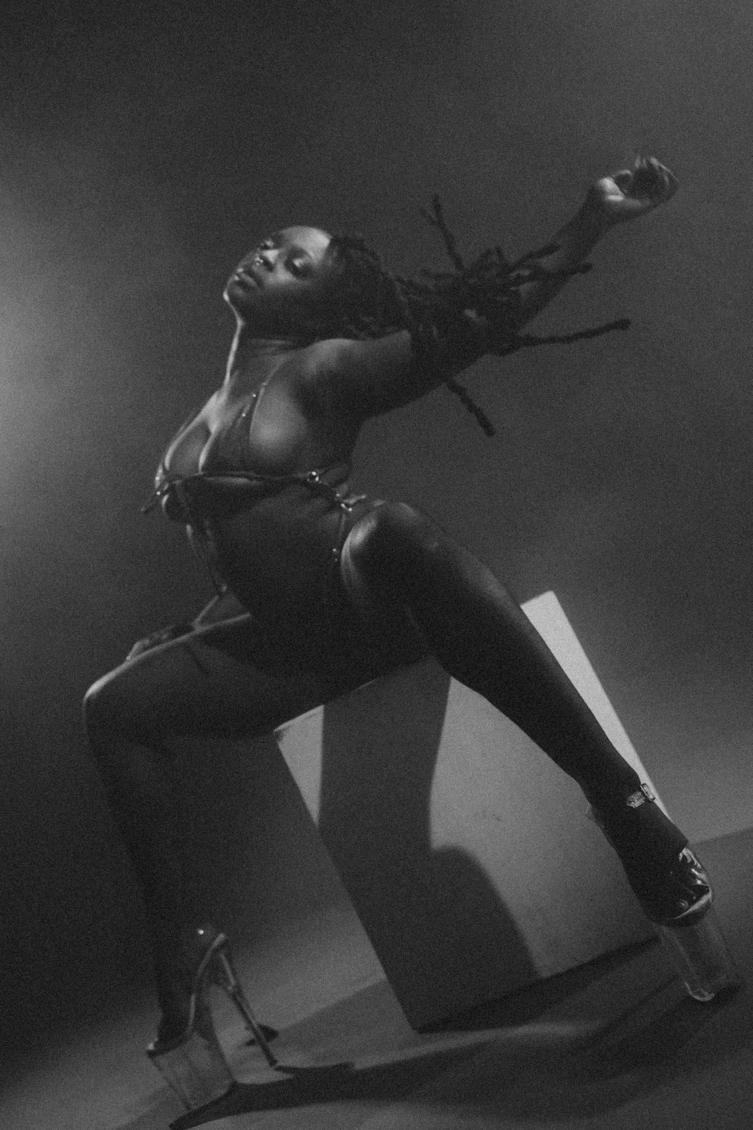 Black and white photo of a dancer in lingerie posing dramatically with high heels on stage.