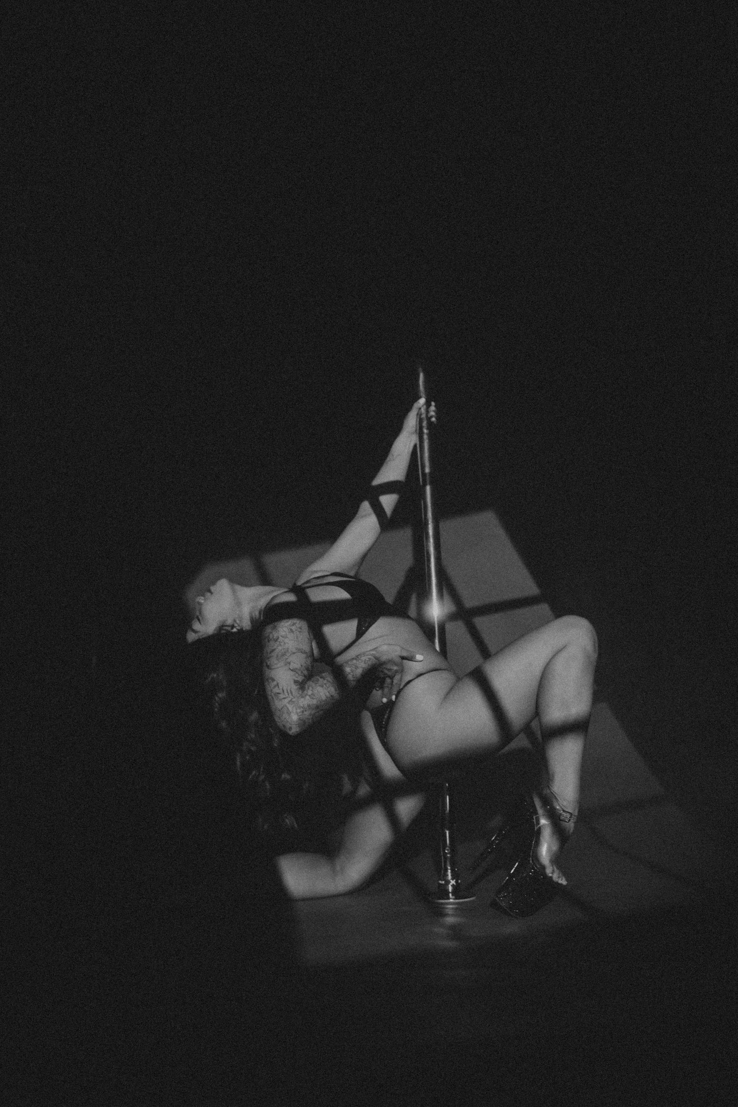 Black and white photo of a pole dancer performing a dramatic floor pose under dramatic stage lighting.