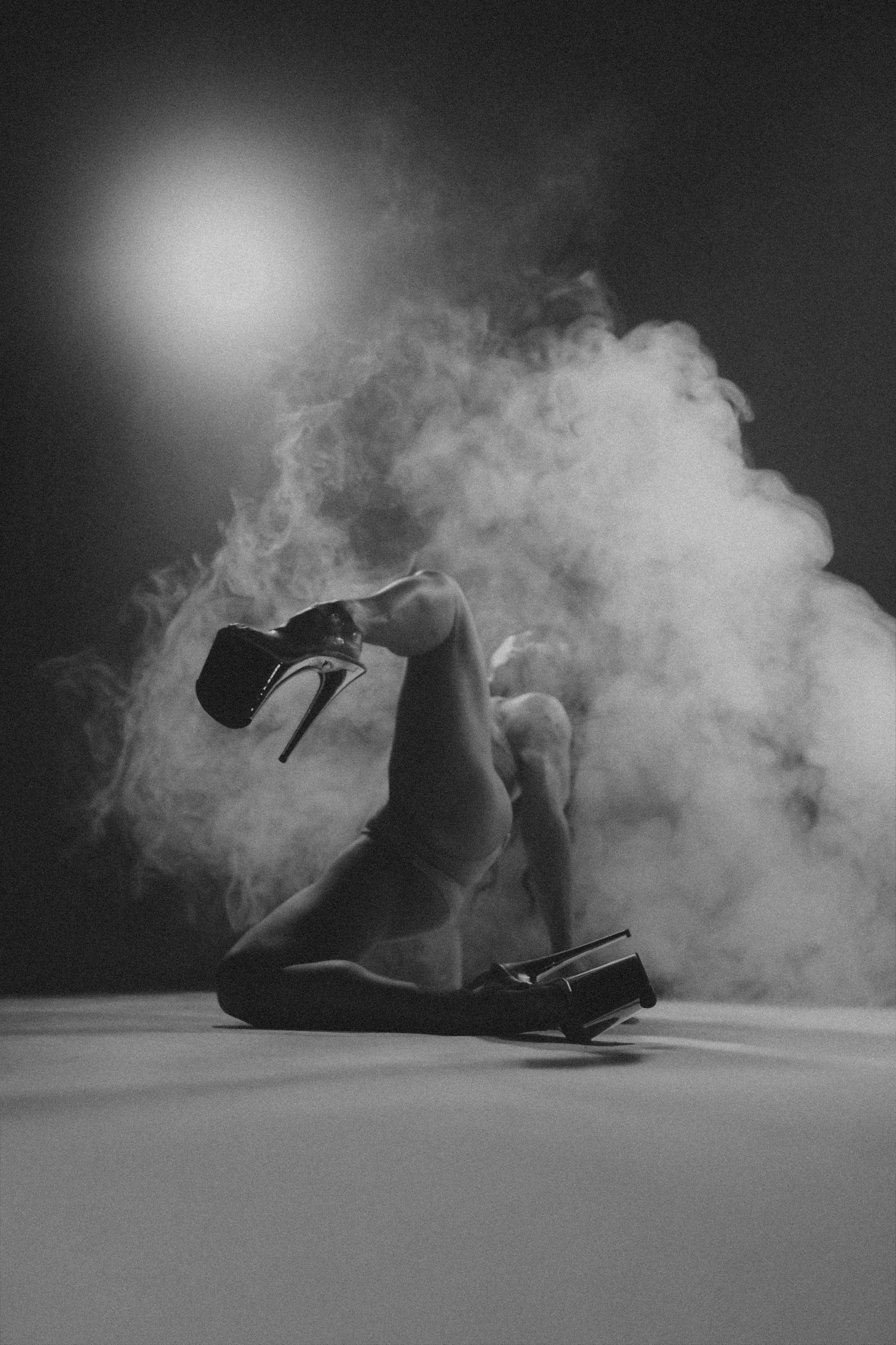 A black and white artistic photo of a dancer posing on the floor surrounded by dramatic smoke.