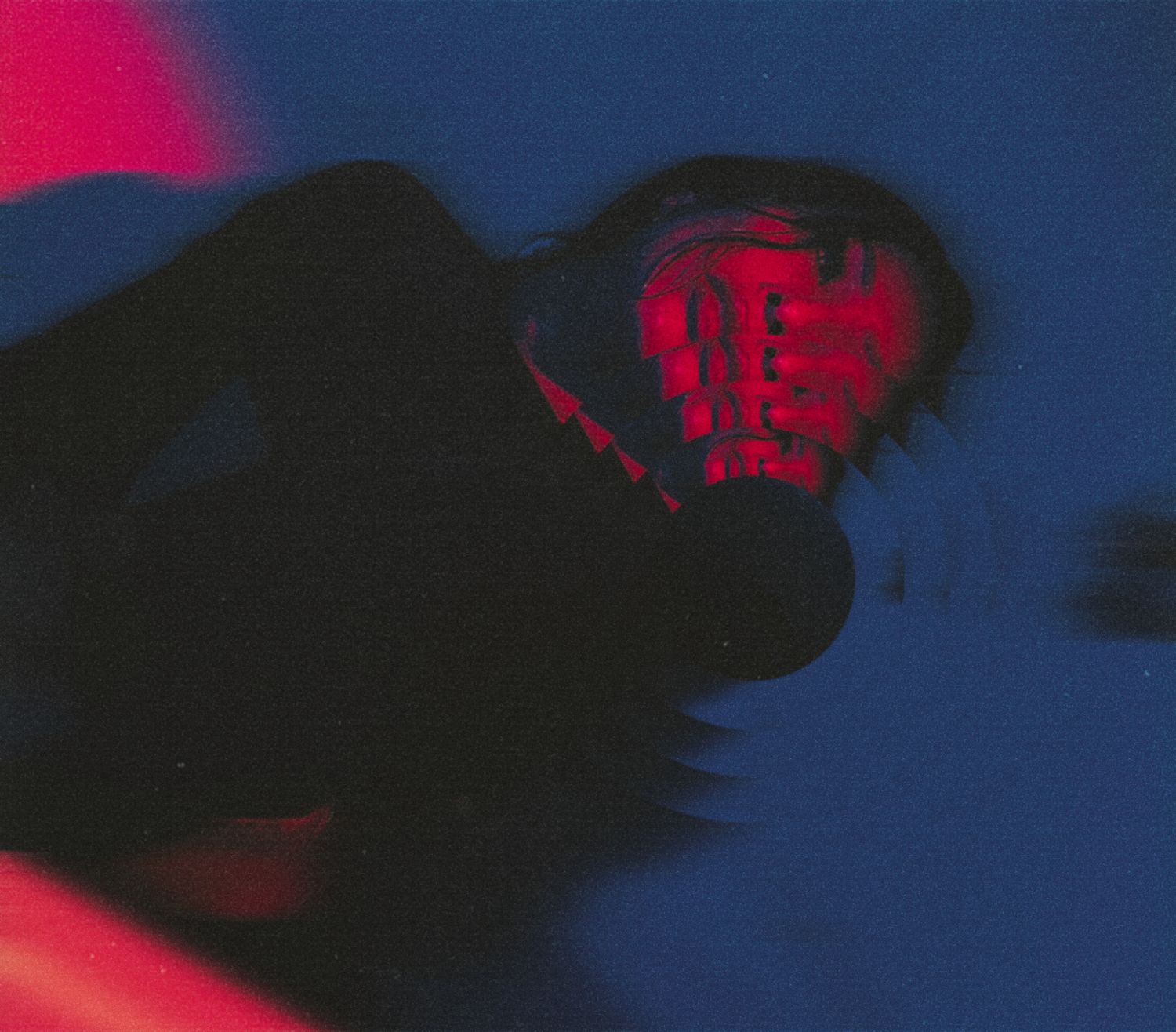 A dramatic portrait with deep blue tones and a striking red light illuminating a shadowed face.