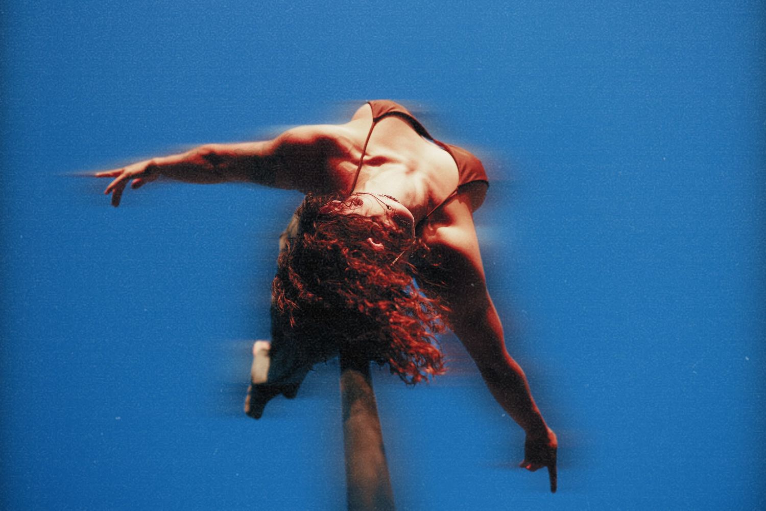 Dynamic aerial pole dancer spinning against a vivid blue sky in a red outfit.
