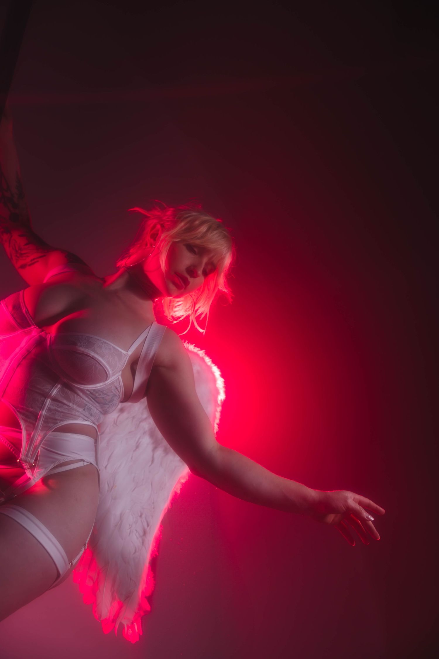 Woman in white angel wings costume posing under dramatic red neon lighting in a nightclub.