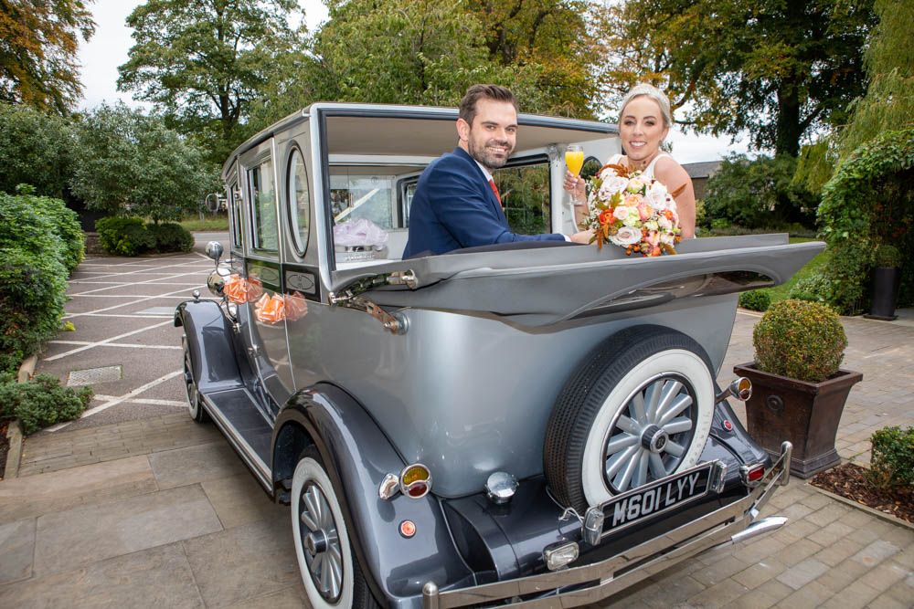 Bride and groom posing in a vintage grey wedding car with floral decorations.