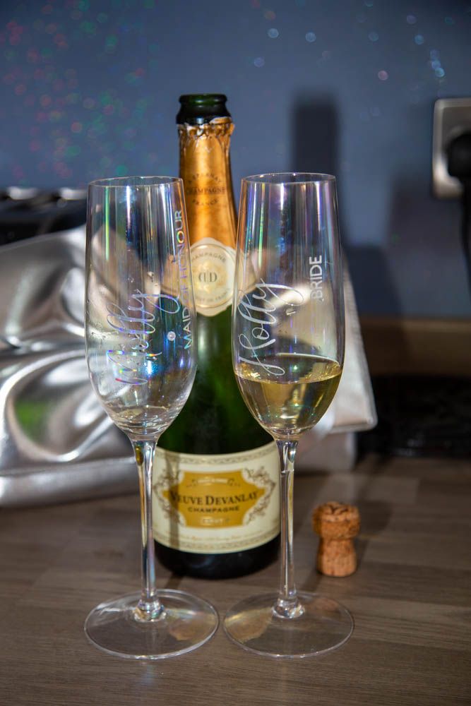 Two personalized champagne flutes labeled Bride beside an open Veuve Devanlay champagne bottle with cork on a table.