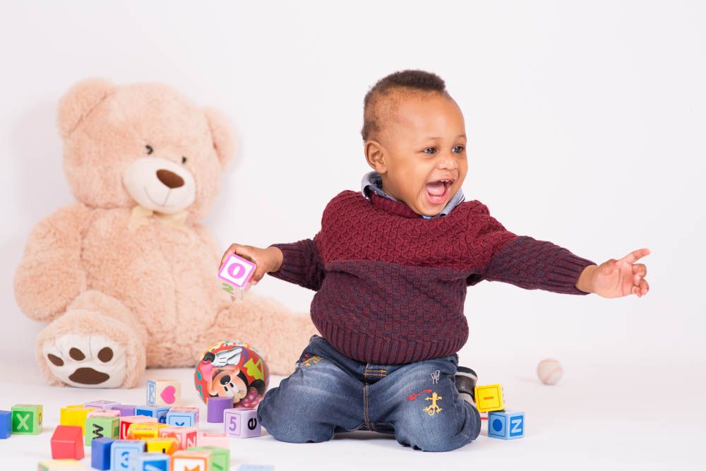 Happy toddler playing with colorful alphabet blocks beside a large teddy bear on white background.