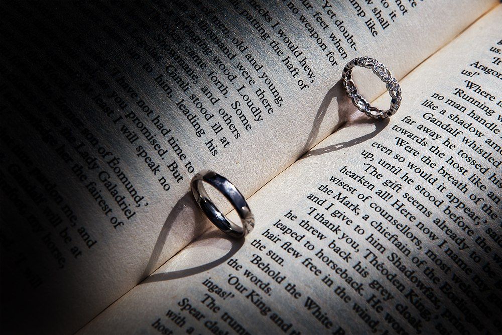 Two wedding rings casting heart-shaped shadows on open book pages in dramatic lighting.