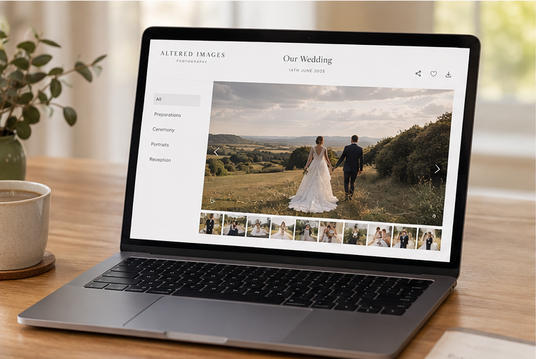 A laptop displaying a wedding photography gallery website with a couple in a field on a wooden desk.