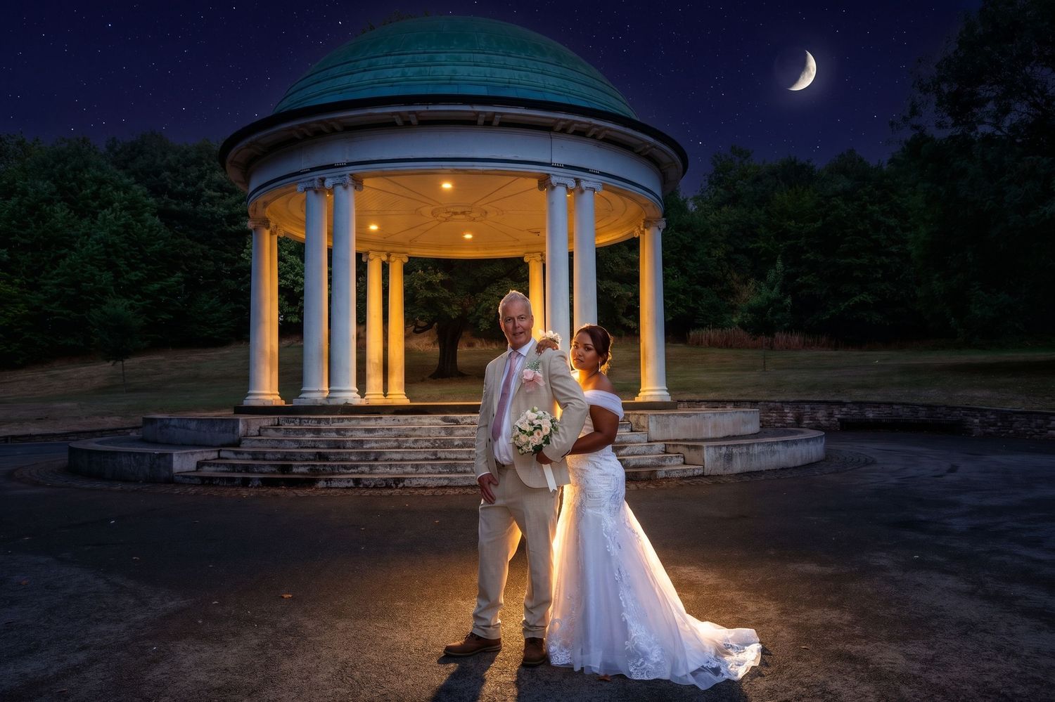 Bride and groom pose romantically before a white gazebo in Clifton Park, Rotherham under a crescent moon at night.