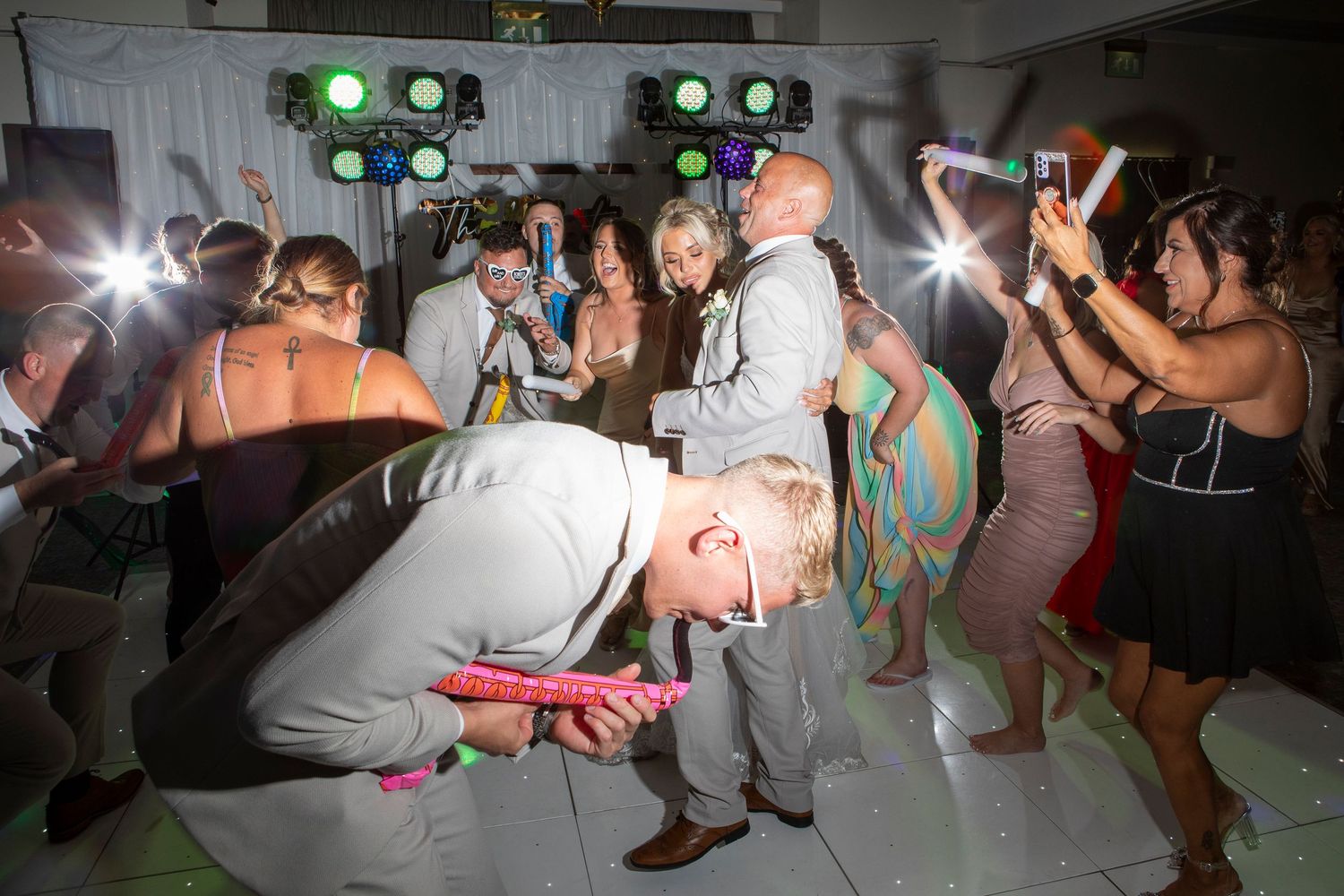 Guests dancing energetically at a wedding reception party with colorful lights and a man doing the limbo.