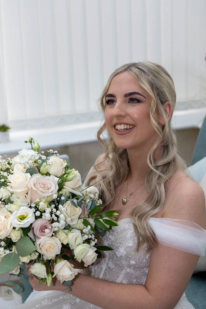 Smiling bride in off-shoulder gown holding elegant white and blush rose bouquet with eucalyptus and baby's breath.