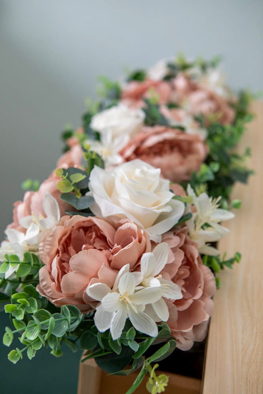 Elegant floral arrangement featuring dusty pink peonies, white roses, and greenery on a wooden surface.