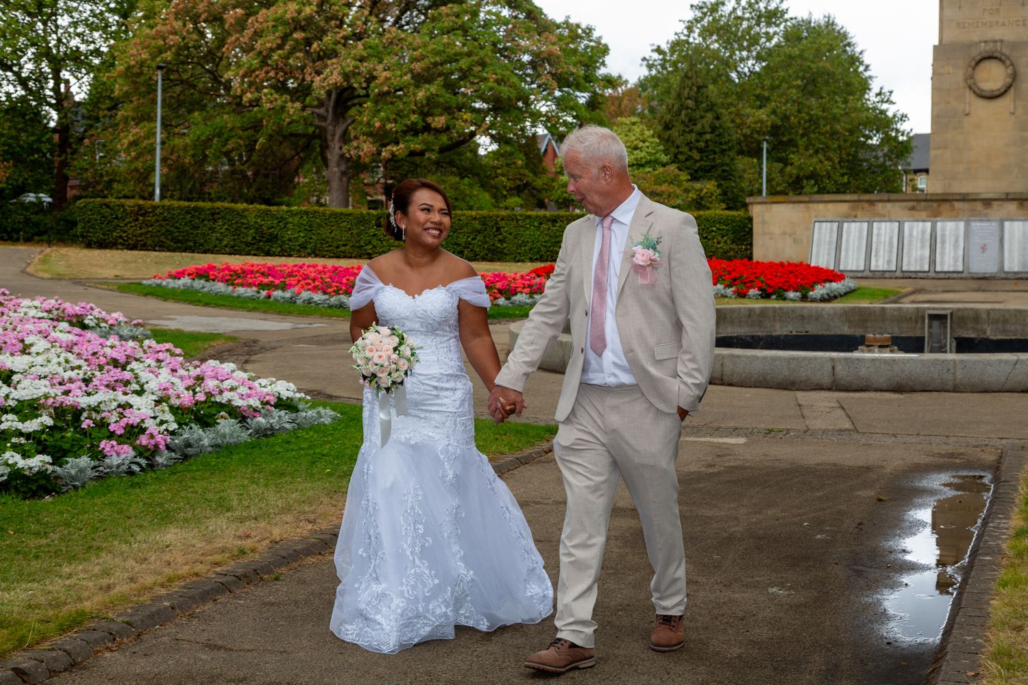 Bride and groom holding hands walking through a colorful garden park on their wedding day.