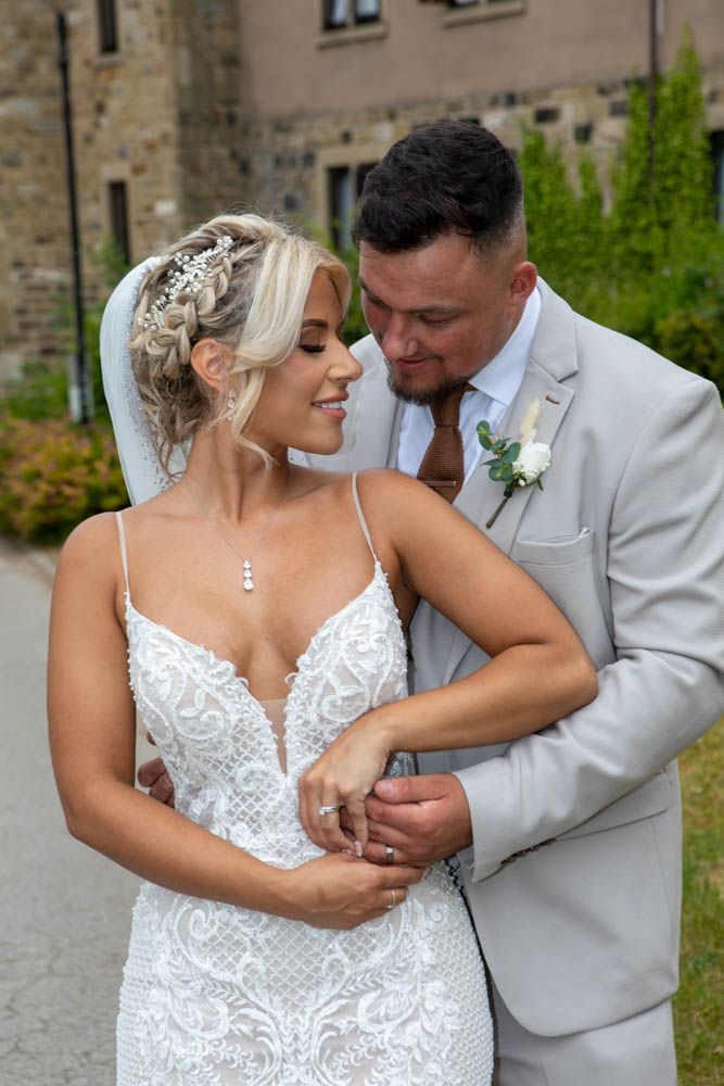 Bride in lace gown and groom in grey suit sharing an intimate moment outdoors.