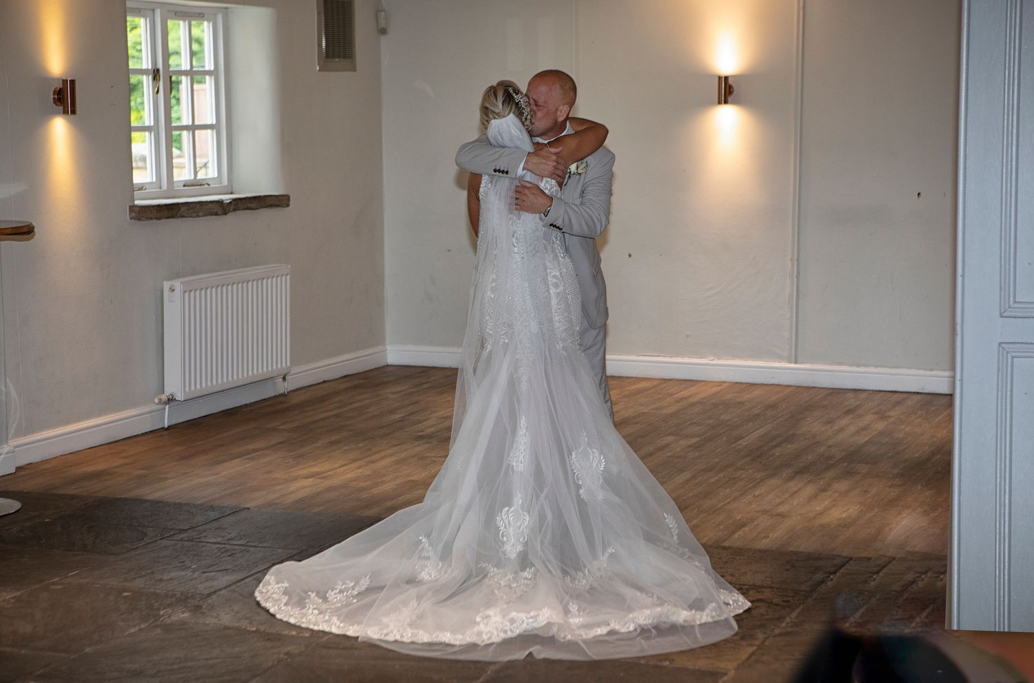 Bride and groom sharing a romantic embrace during their first dance in an elegant wood-floored wedding venue.