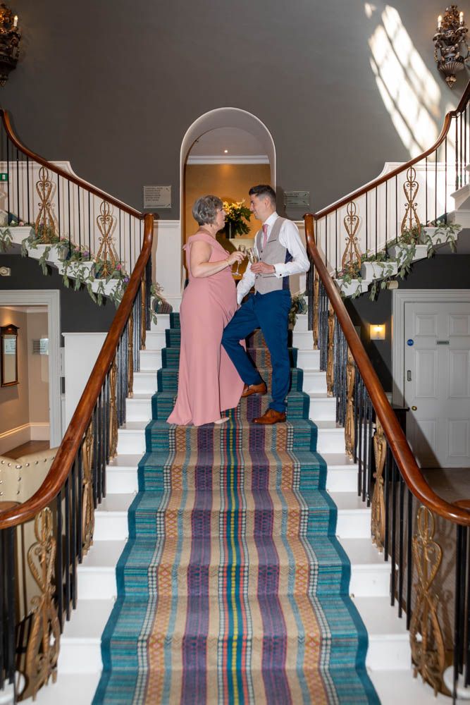 Stephen toasting with champagne on an elegant staircase at Rudding Park Hotel on his wedding morning.