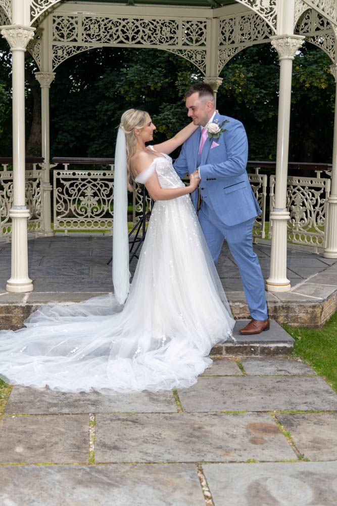Bride and groom share a romantic moment under an ornate white gazebo, bride in flowing white gown with veil.