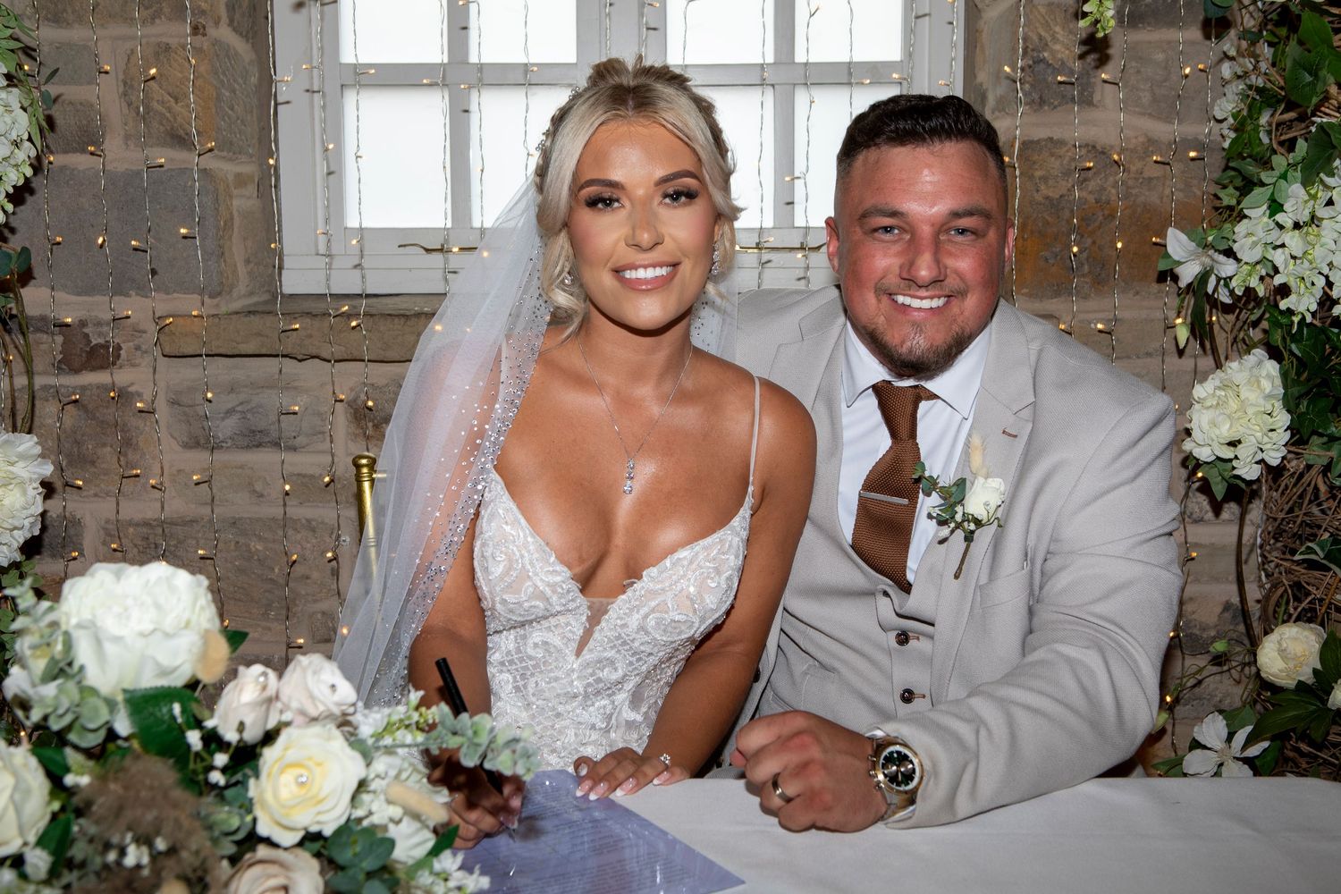 Bride and groom smiling at wedding table with white floral arrangements in elegant stone venue.