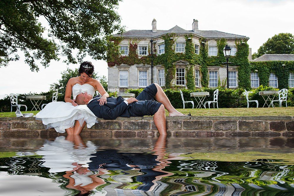 Bride and groom in a romantic dip pose reflected in water before an ivy manor.