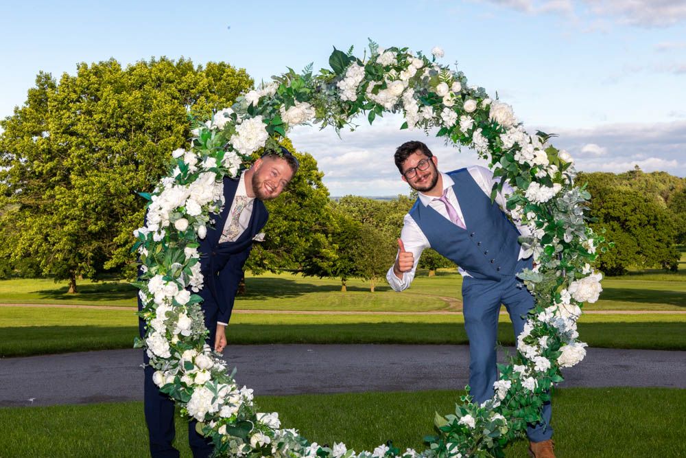 Two wedding guest posing under a circular white floral arch overlooking the golf course at Rudding House, Rudding Park Hotel.