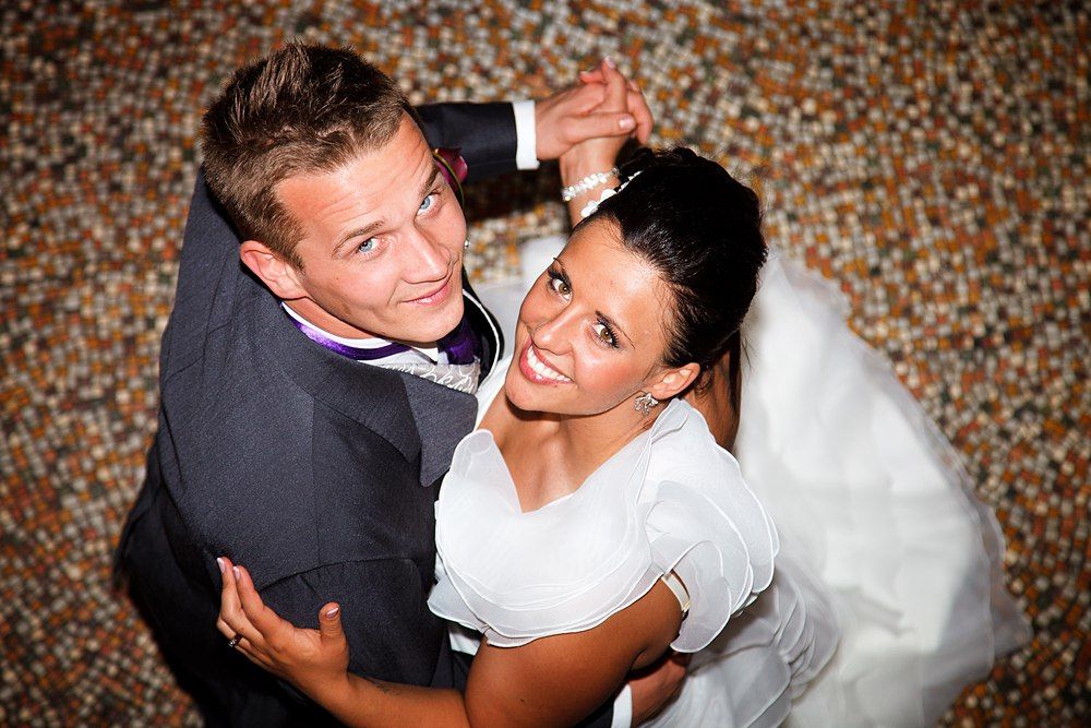 Happy bride and groom share first dance, smiling joyfully at wedding reception with bokeh background.