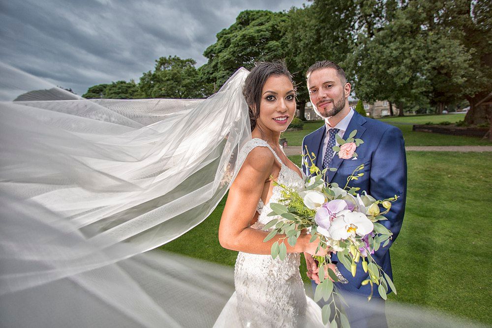 Bride with flowing veil and groom in navy suit posing with a floral bouquet.