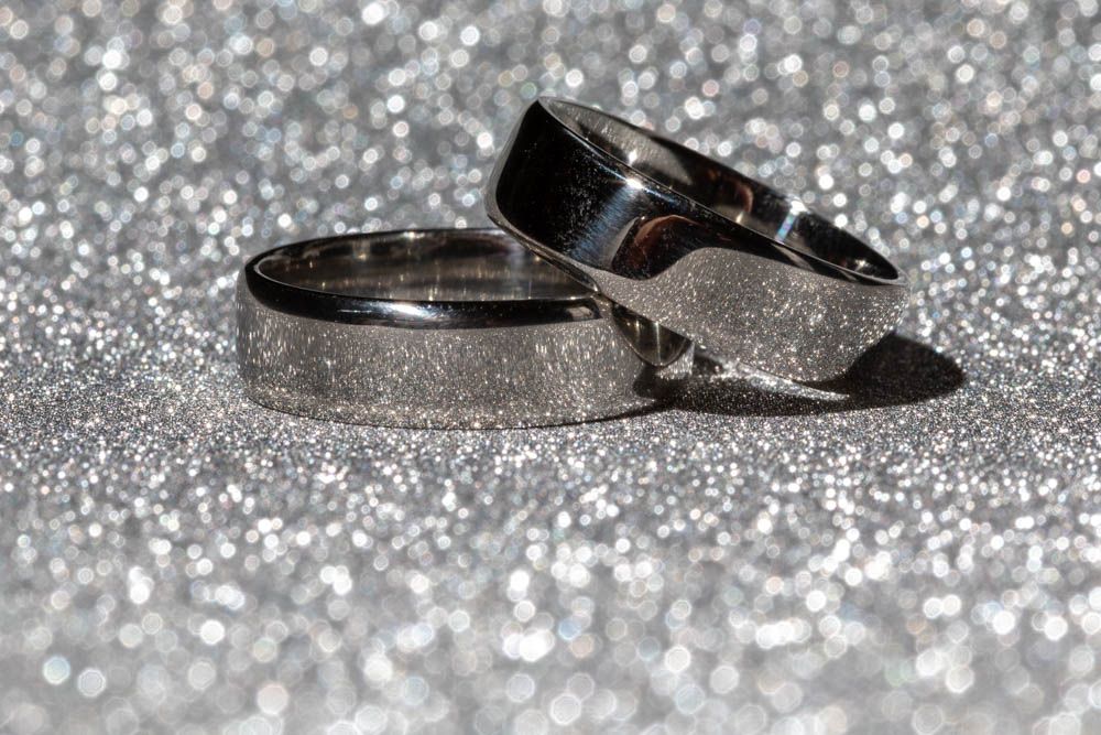 Two silver wedding bands resting on a sparkling glitter surface.