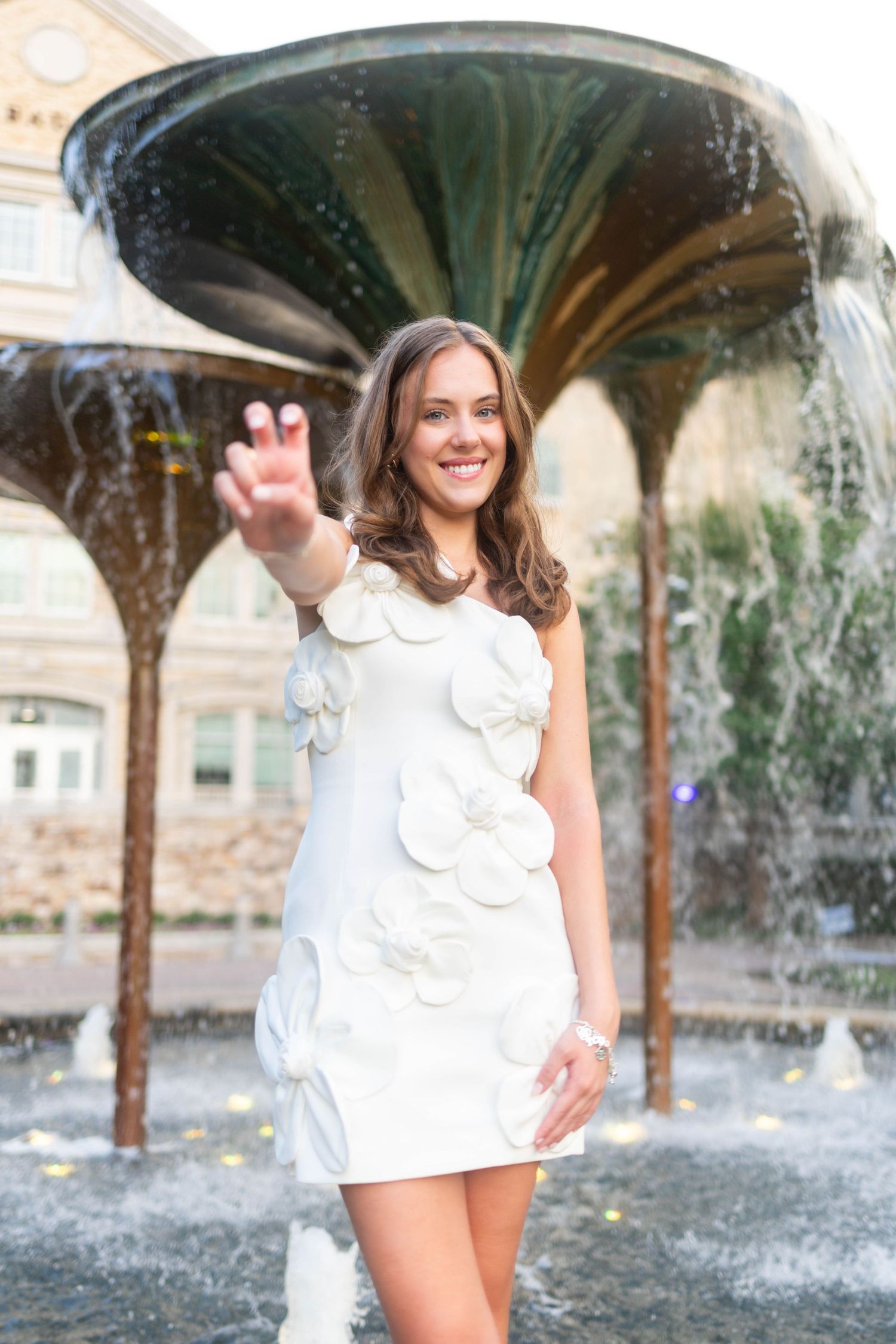 Young woman in white floral dress posing by decorative fountain.