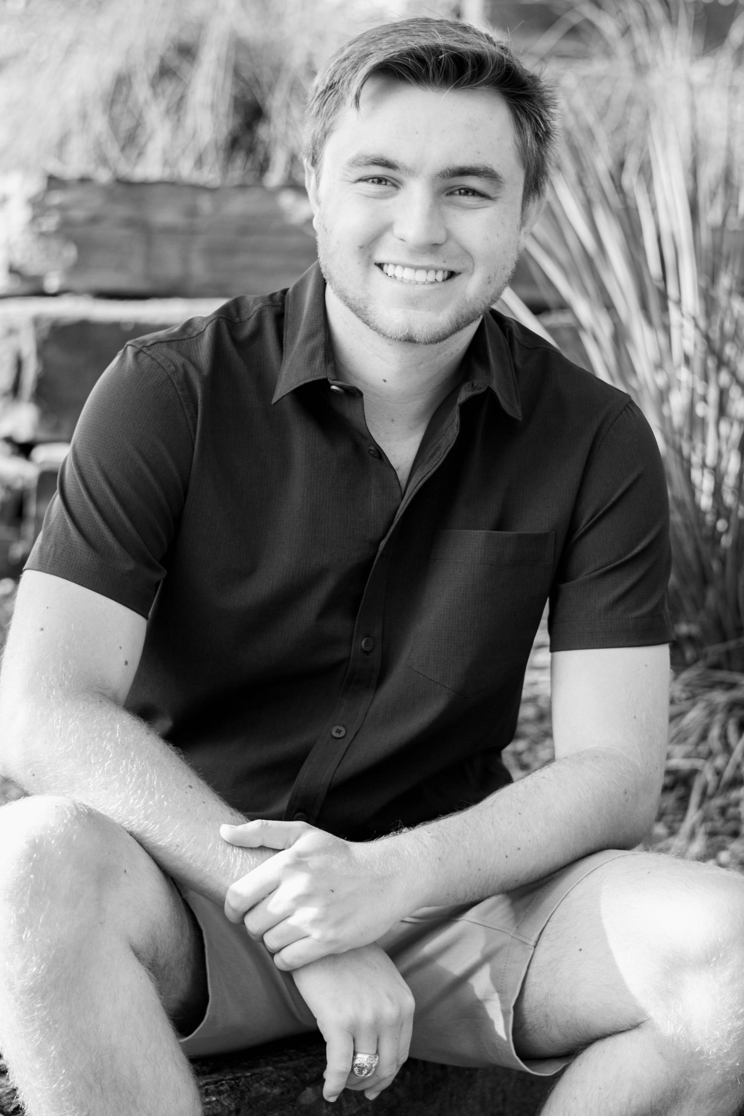 Smiling young man in dark polo shirt sitting outdoors in black and white portrait photo.