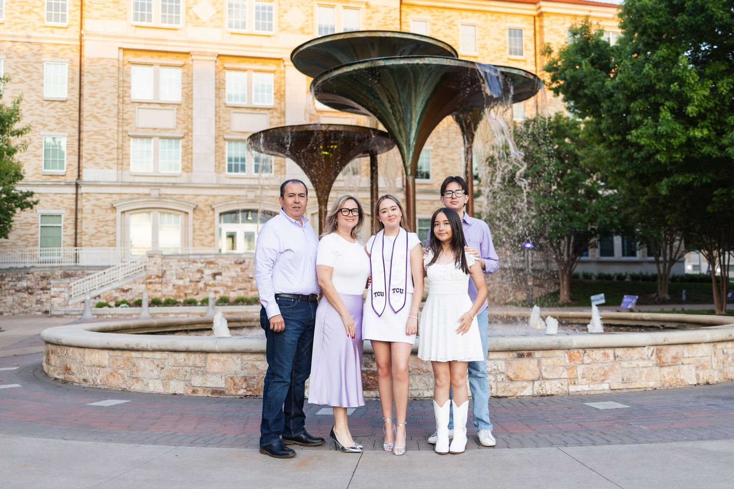 Family of five posing in front of a decorative fountain outside a brick university building during a graduation celebration.