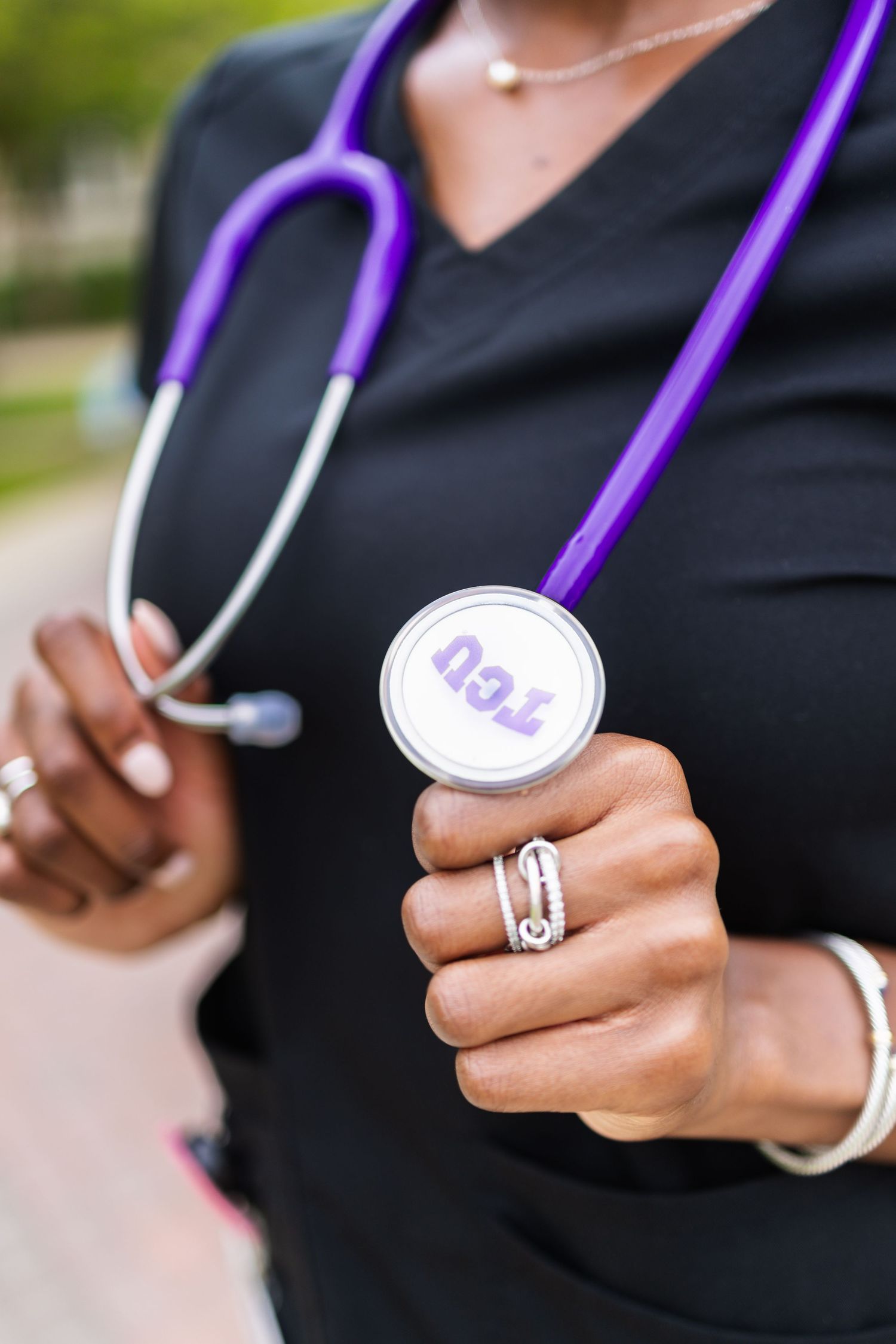 Close-up of a TCU nursing graduate holding a purple stethoscope with the TCU logo visible.