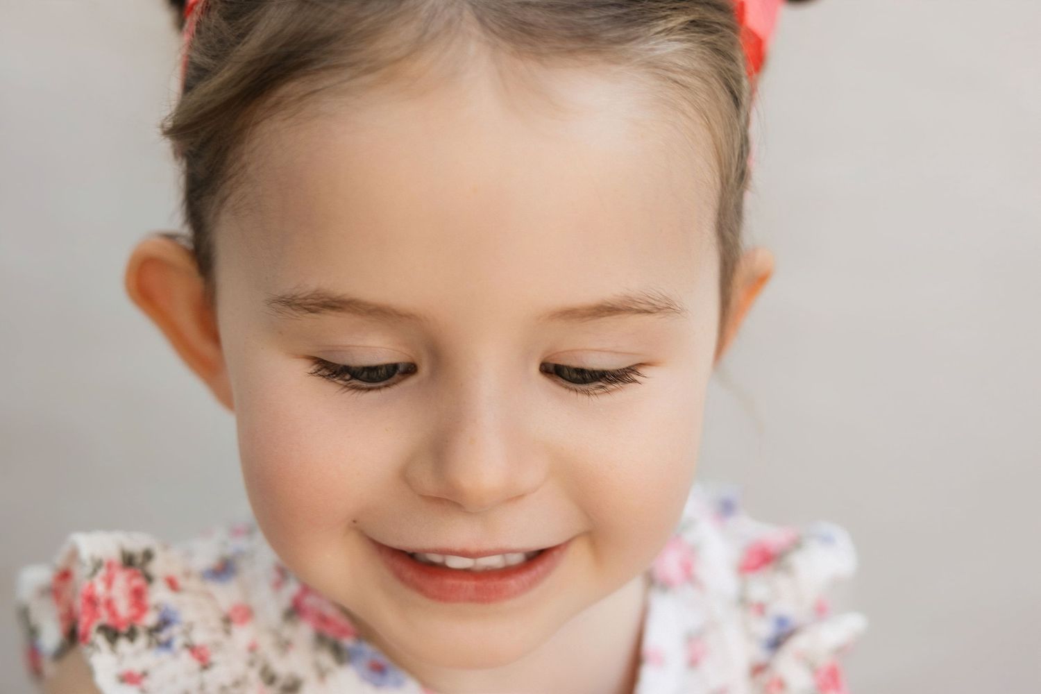 Close-up portrait of a smiling young girl with a red bow in her hair wearing a floral top.