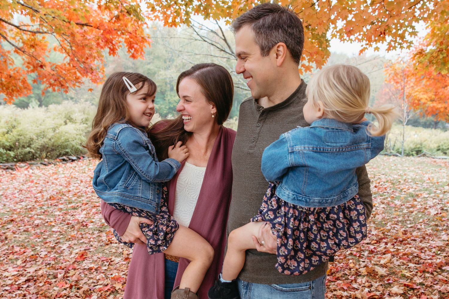 Joyful family of four laughing together surrounded by vibrant red autumn foliage.