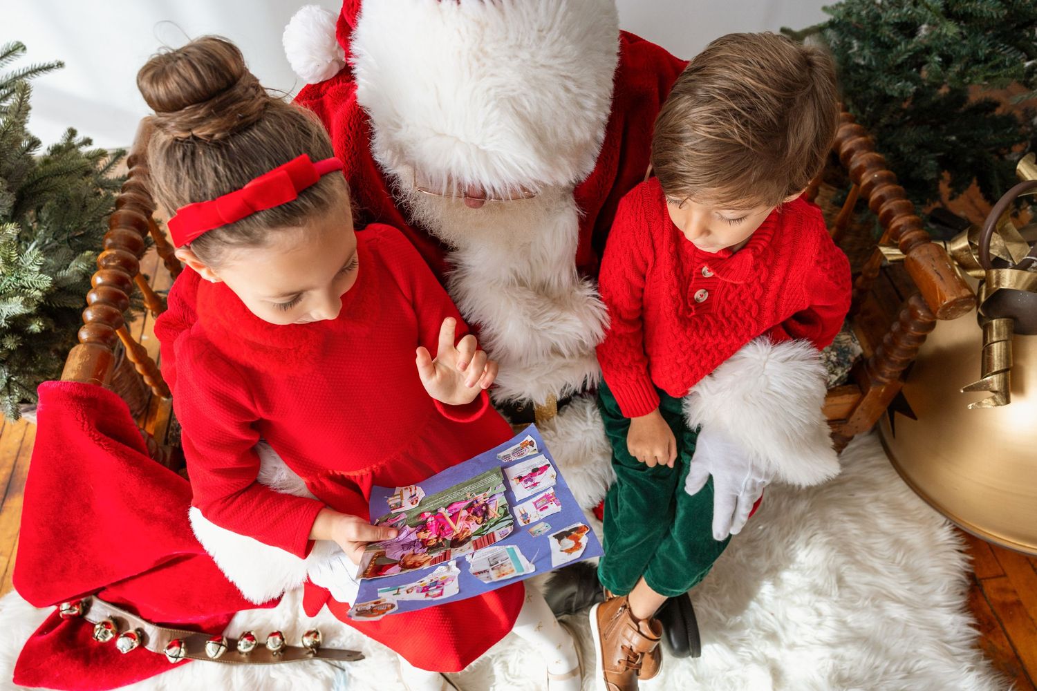 Two children in red outfits sit with Santa Claus looking at a book during a Christmas portrait session.
