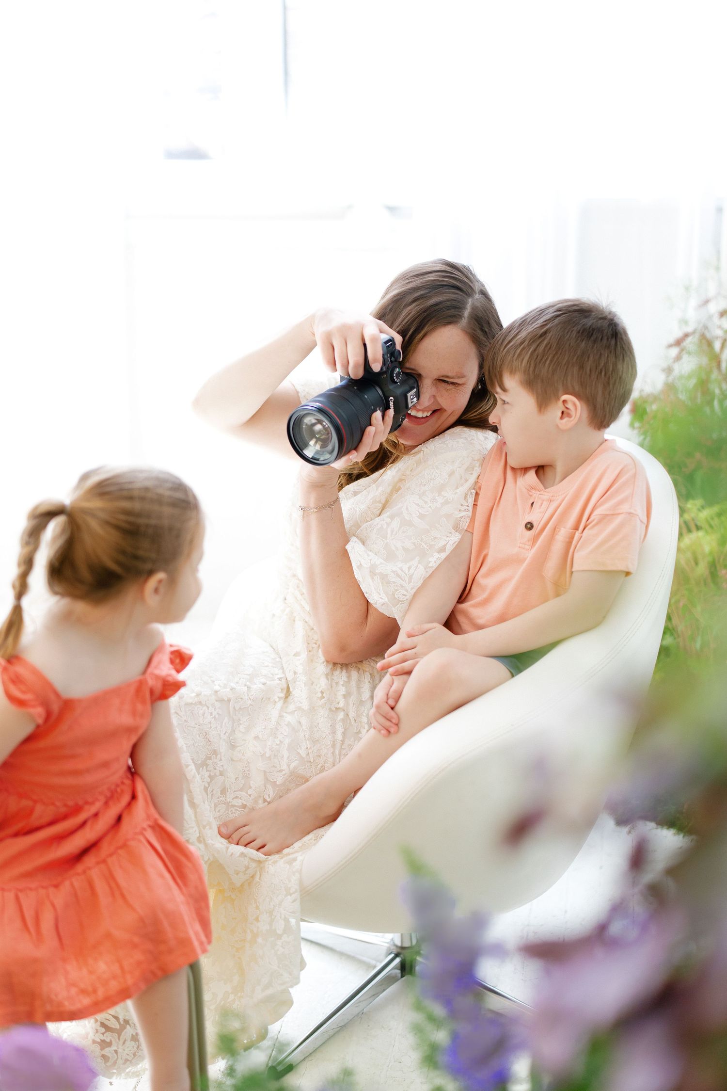 Hilary Mauro in white dress taking photos with two children in bright studio setting.