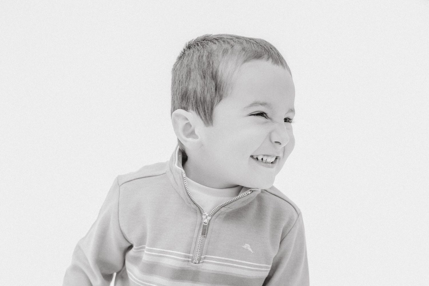 Laughing young boy in striped jacket captured in expressive black and white portrait.