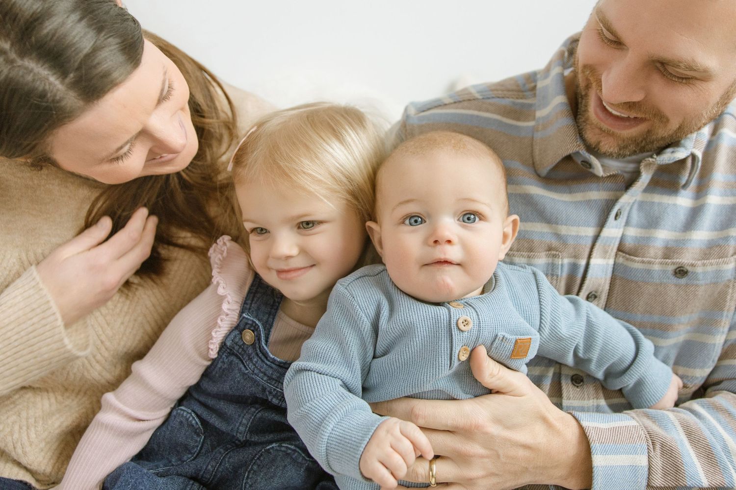 Happy young family of four with two small children snuggling together during a cozy indoor portrait session.