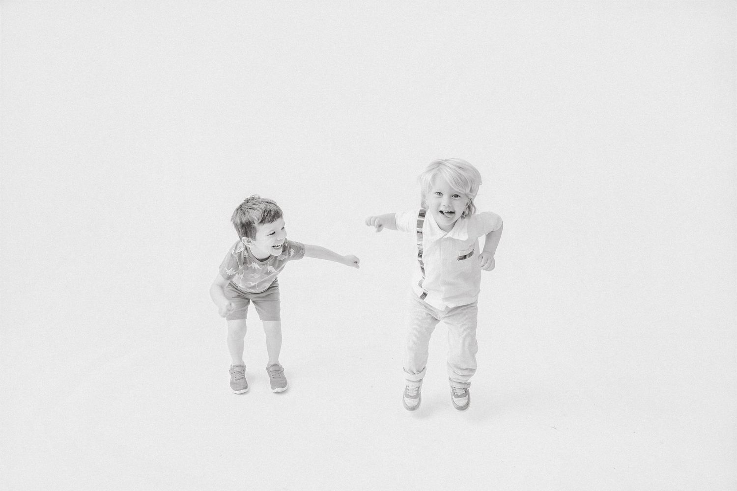 Two playful children pointing at each other in a fun black and white studio photo.