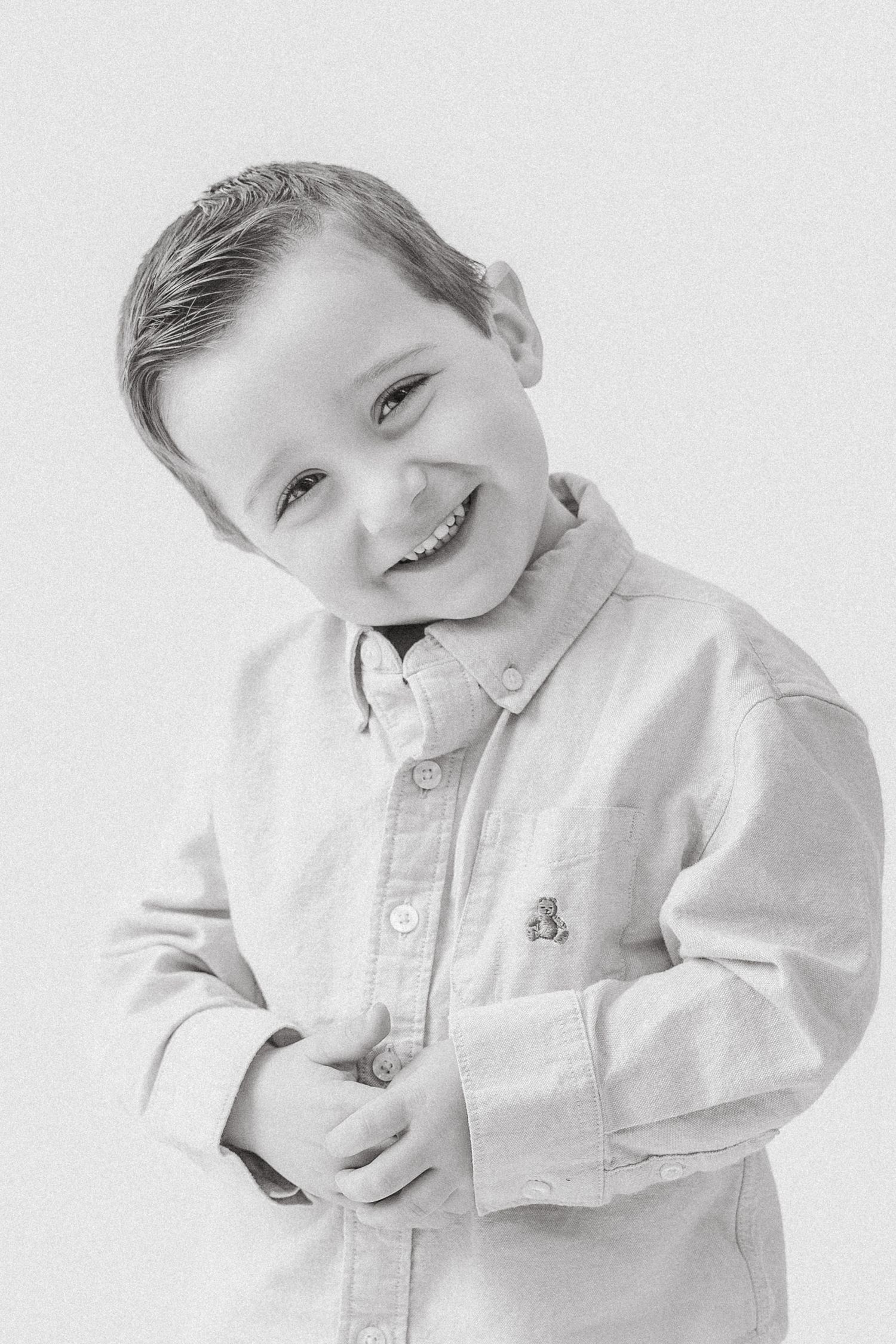Adorable young boy in a button-up shirt smiling joyfully in a black and white portrait.