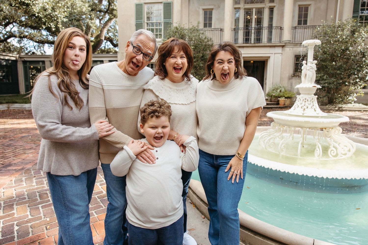 Joyful family of five making funny faces together near a fountain outside a grand estate.