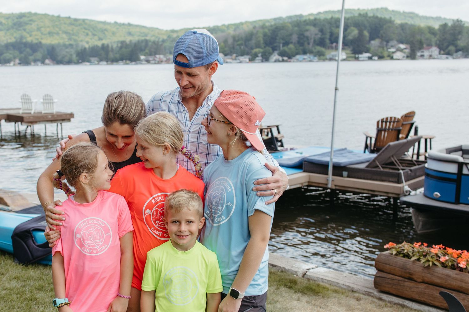 Happy family of six posing together near a lakeside dock on a summer day.